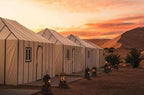 Merzouga VIP Luxury Camp beige canvas tents with striped patterns and lanterns at desert sunset with sand dunes