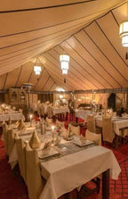 Merzouga VIP Luxury Camp dining tent with beige fabric walls and ceiling, decorated with elegant lanterns and neatly set tables