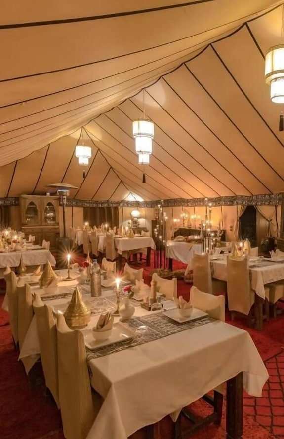 Merzouga VIP Luxury Camp dining tent with beige fabric walls and ceiling, decorated with elegant lanterns and neatly set tables