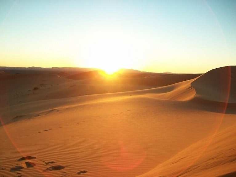 Merzouga VIP Luxury Camp view of golden sand dunes at sunset with smooth ripples and a bright horizon