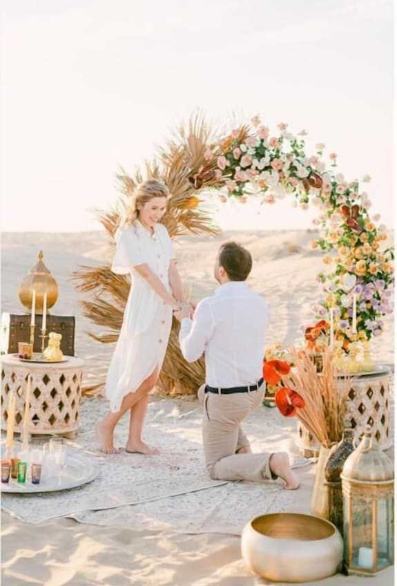 Merzouga VIP Luxury Camp romantic desert proposal setup with floral arch, golden lanterns, and decorative rugs on sand
