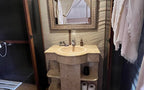Bathroom sink with beige stone countertop and ornate framed mirror, towels hanging and toilet paper visible, Moonlight luxury Desert Camp