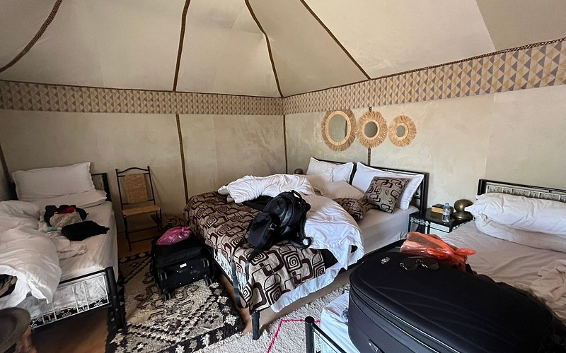 Moonlight luxury Desert Camp bedroom with three beds, patterned brown and white bedding, beige fabric tent walls, and decorative wall hangings