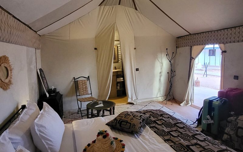 Moonlight luxury Desert Camp beige fabric tent interior with bed, patterned pillows, small table, and open entrance door