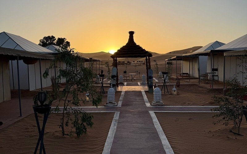 Moonlight luxury Desert Camp featuring beige canvas tents with white trim, a central covered seating area, and lanterns at sunset in the desert