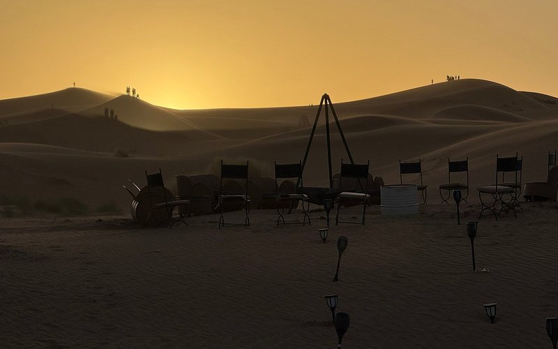 Moonlight luxury Desert Camp setting with silhouetted chairs arranged in a desert at sunset with sand dunes in the background