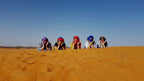 Moonlight luxury Desert Camp visitors with colorful headscarves lying on golden desert sand under clear blue sky