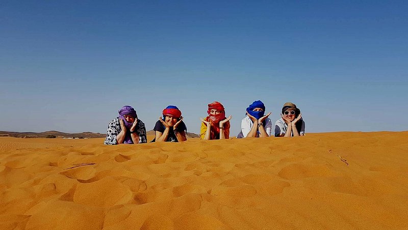 Moonlight luxury Desert Camp visitors with colorful headscarves lying on golden desert sand under clear blue sky