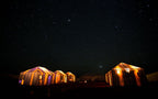 Moonlight luxury Desert Camp tents glowing warmly under a star-filled night sky in the desert