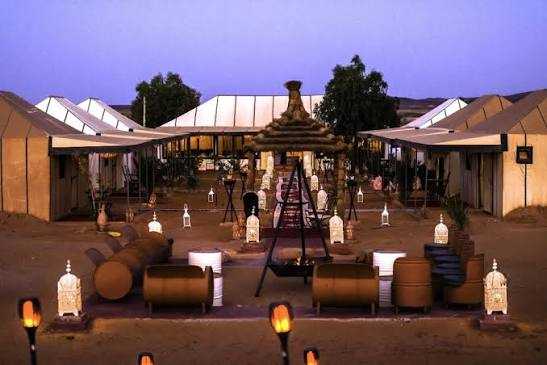Moonlight luxury Desert Camp featuring large beige canvas tents with peaked roofs, outdoor seating, and Moroccan lanterns at dusk