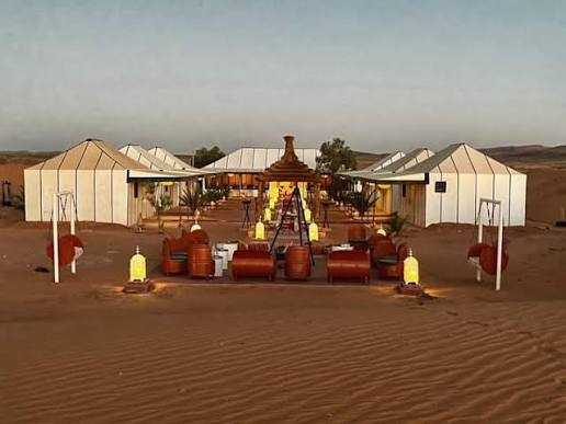Moonlight luxury Desert Camp features spacious white canvas tents on a sandy desert landscape with traditional lanterns and seating areas.