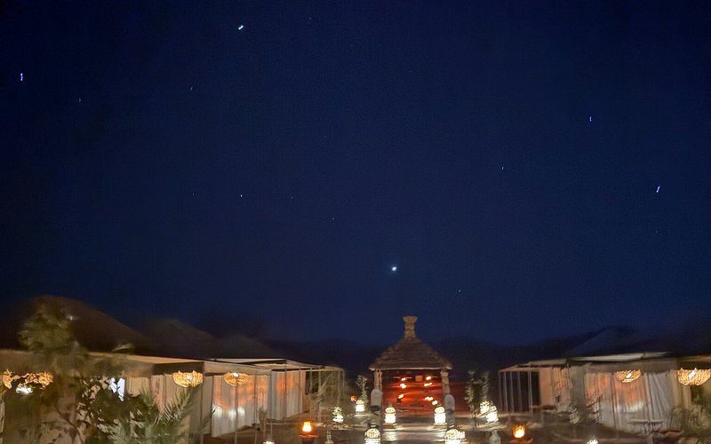 Moonlight luxury Desert Camp at night with illuminated traditional tents and lanterns under a starry sky in the desert