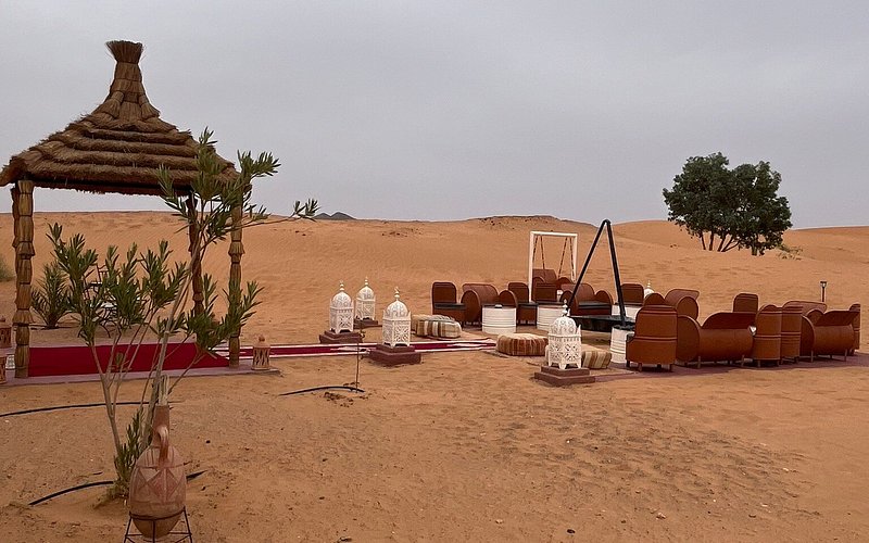 Moonlight luxury Desert Camp open seating area in the Moroccan Sahara with brown leather chairs, striped cushions, and white lanterns on sand