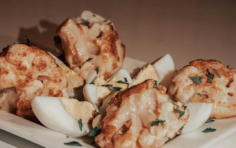 Close-up of golden-browned roasted cauliflower florets and quartered boiled eggs garnished with chopped herbs on a white plate, representing a dish from Moonlight luxury Desert Camp