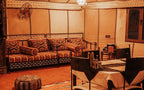 Moonlight luxury Desert Camp interior with traditional patterned brown and beige cushions on wooden sofa, round pouf, and dining table with chairs