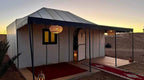 White luxury tent with black trim and exterior lanterns at dusk in desert setting, showcasing Moonlight luxury Desert Camp