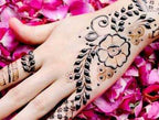 Moroccan Henna Tattoo on hand featuring intricate black floral and leafy patterns with delicate swirling details on pink petals.
