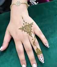 Moroccan Henna Tattoo on a hand featuring a triangular geometric pattern in brown henna with detailed dots and lines.