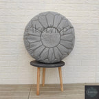 Moroccan pouf in gray leather with decorative stitching and intricate central embroidery, round and handmade