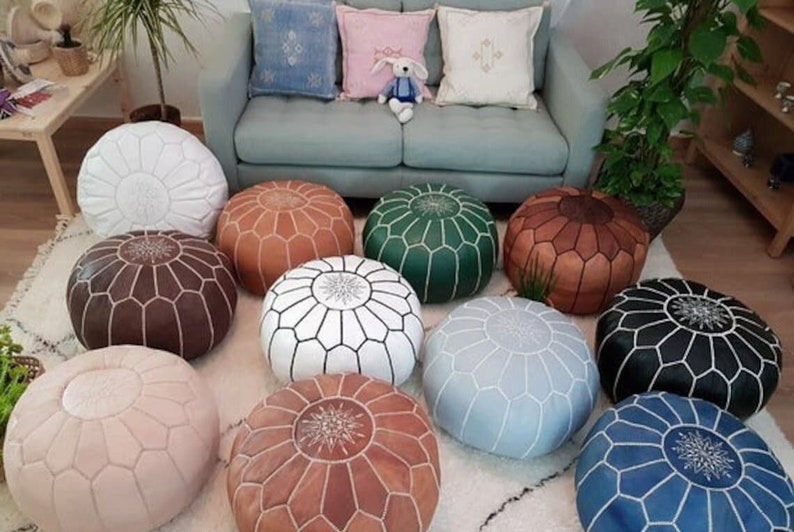 Moroccan pouf collection featuring round handmade leather ottomans in various colors including white, brown, green, black, blue, and tan with stitched geometric patterns
