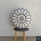 Round Moroccan pouf in white fabric with black embroidered geometric patterns and central star design, placed on a wooden stool