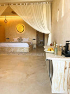 Nasser Palace Suites & Spa bedroom featuring beige stone textured walls, a canopy bed with white curtains, and a decorative fruit tray on a marble counter