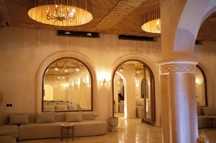 Interior lounge of Nasser Palace Suites & Spa with beige walls, arched mirrors, cushioned beige sofas, and warm lighting