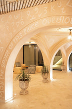 Nasser Palace Suites & Spa interior featuring beige arched ceilings with white script art, tiled floors, plants in ornate pots, and patterned cushions