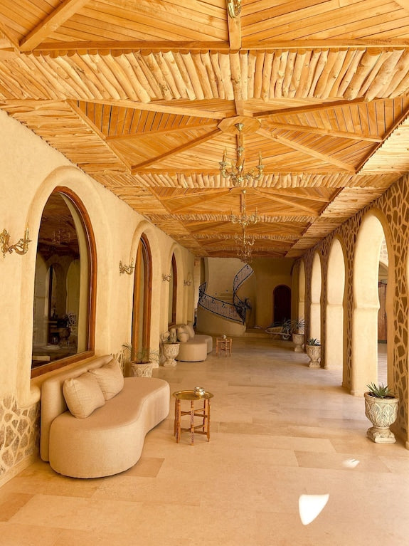 Nasser Palace Suites & Spa corridor with beige stone flooring, arched doorways, ornate wooden ceiling, curved beige seating, and small tables