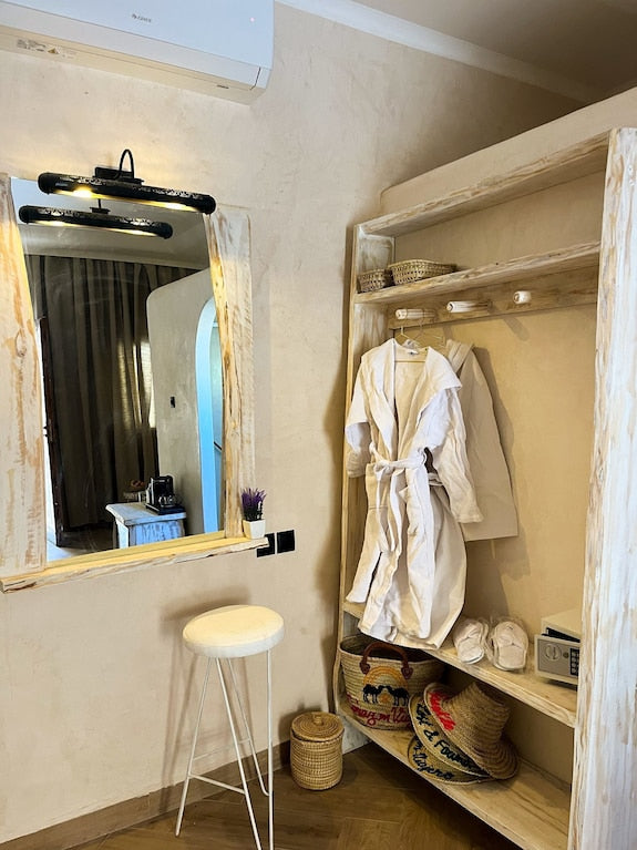 Nasser Palace Suites & Spa cozy beige room corner with wooden shelves, white bathrobes, slippers, and a large mirror