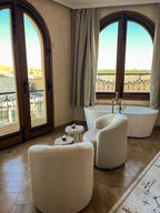 Nasser Palace Suites & Spa room with cream upholstered chairs, wooden floor, white freestanding bathtub, and arched windows with wrought iron railings