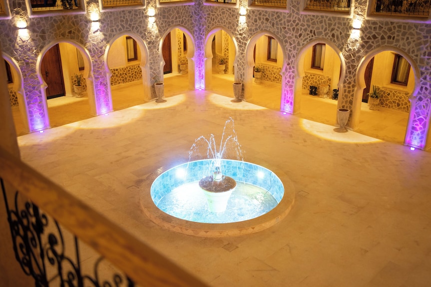 Nasser Palace Suites & Spa Moroccan courtyard with stone archways, warm lighting, and illuminated central water fountain
