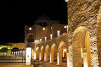 Nasser Palace Suites & Spa illuminated at night featuring warm stone arches and traditional Moroccan architecture under a black sky