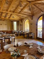 Nasser Palace Suites & Spa restaurant interior with rustic wooden ceiling, stone walls, and neatly set dining tables with plates and glassware