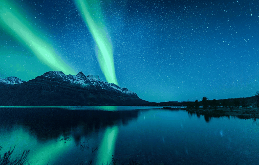 Norway Tromso fjord landscape with snow-capped mountains and vivid green northern lights reflected on calm water