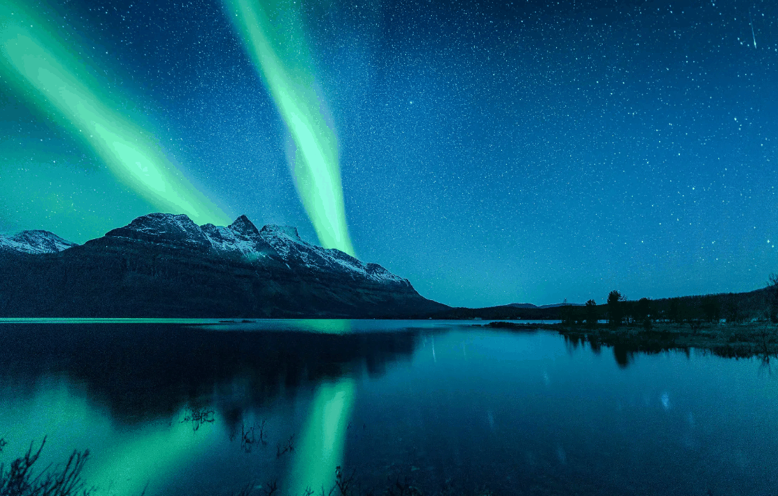 Norway Tromso fjord landscape with snow-capped mountains and vivid green northern lights reflected on calm water