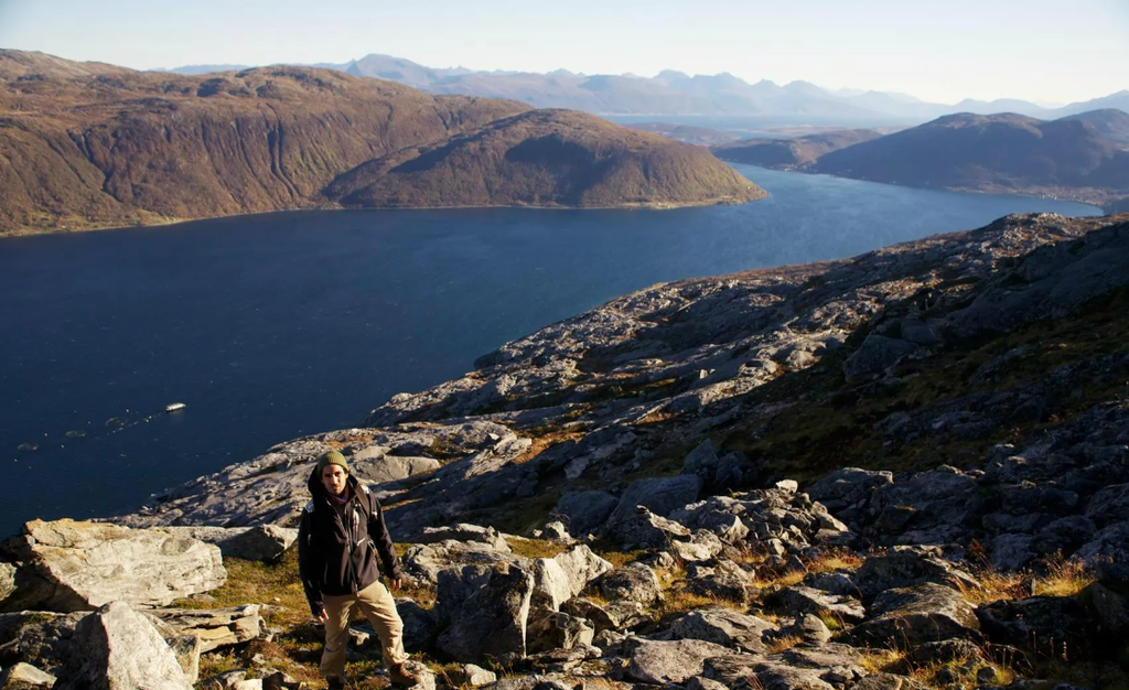 Norway Tromso fjord landscape with rugged rocky shoreline, deep blue water, mountains, and hiker