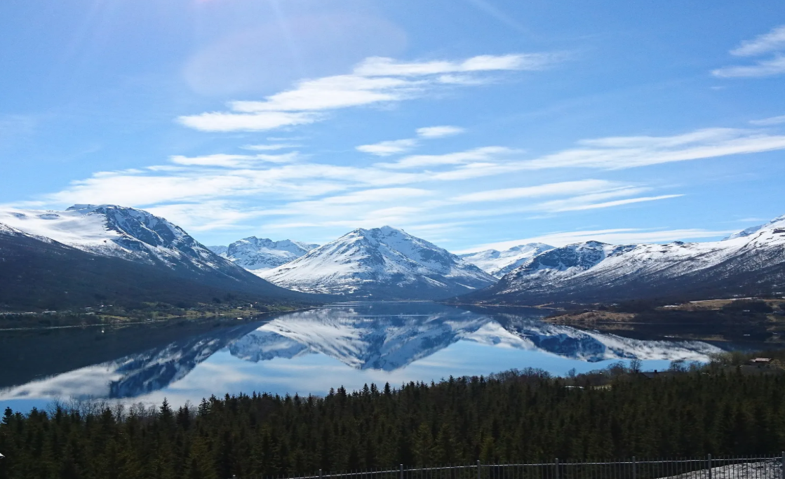 Norway Tromso fjord landscape with snow-capped mountains, calm reflective water, and evergreen forest