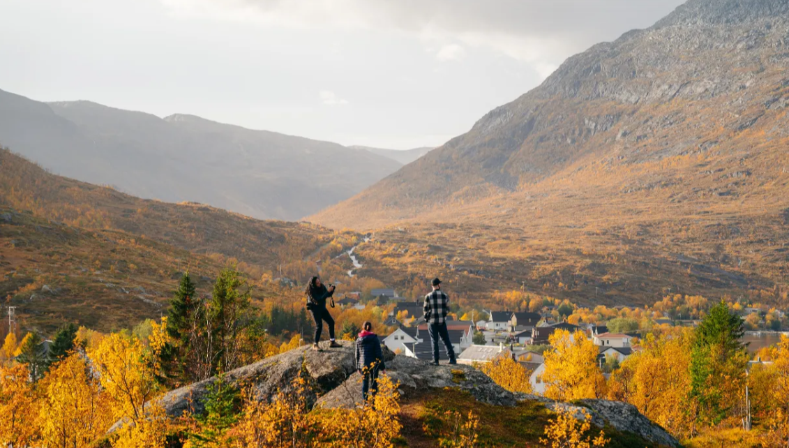 Norway Tromso fjord tour with hikers overlooking an autumn valley village beneath rugged golden mountains