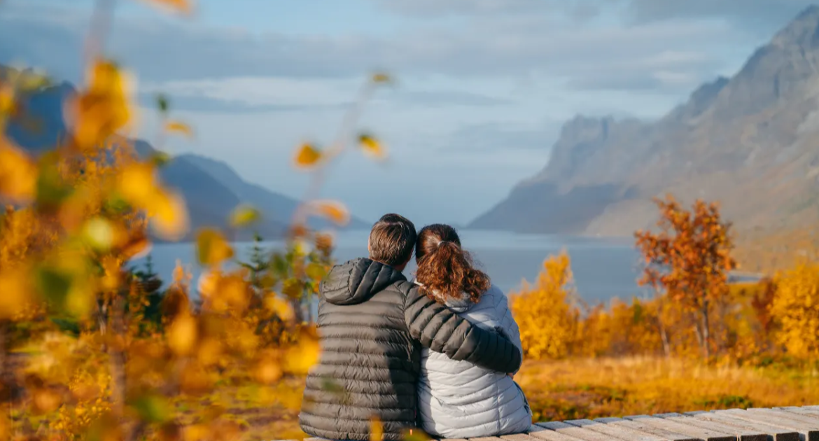 Norway Tromso fjord tour with couple in grey jackets overlooking autumn mountains and blue water