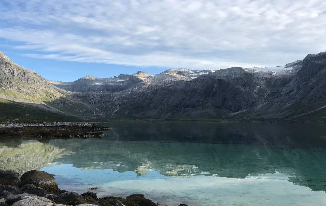 Norway Tromso fjord landscape with turquoise lake, rocky shoreline, rugged mountains, and glacial snowfields