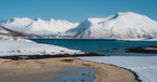 Norway Tromso fjord with turquoise water, snowy mountains, sandy beach and icy shoreline