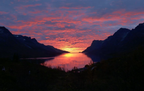 Norway Tromso fjord with dark mountain silhouettes and a vivid pink and orange sunset reflected on calm water