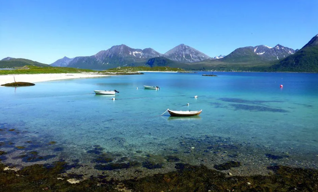 Norway Tromso fjord with turquoise water, white sandy beach, small boats, and rugged snow-capped mountains