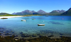 Norway Tromso fjord with turquoise water, white sandy beach, small boats, and rugged snow-capped mountains