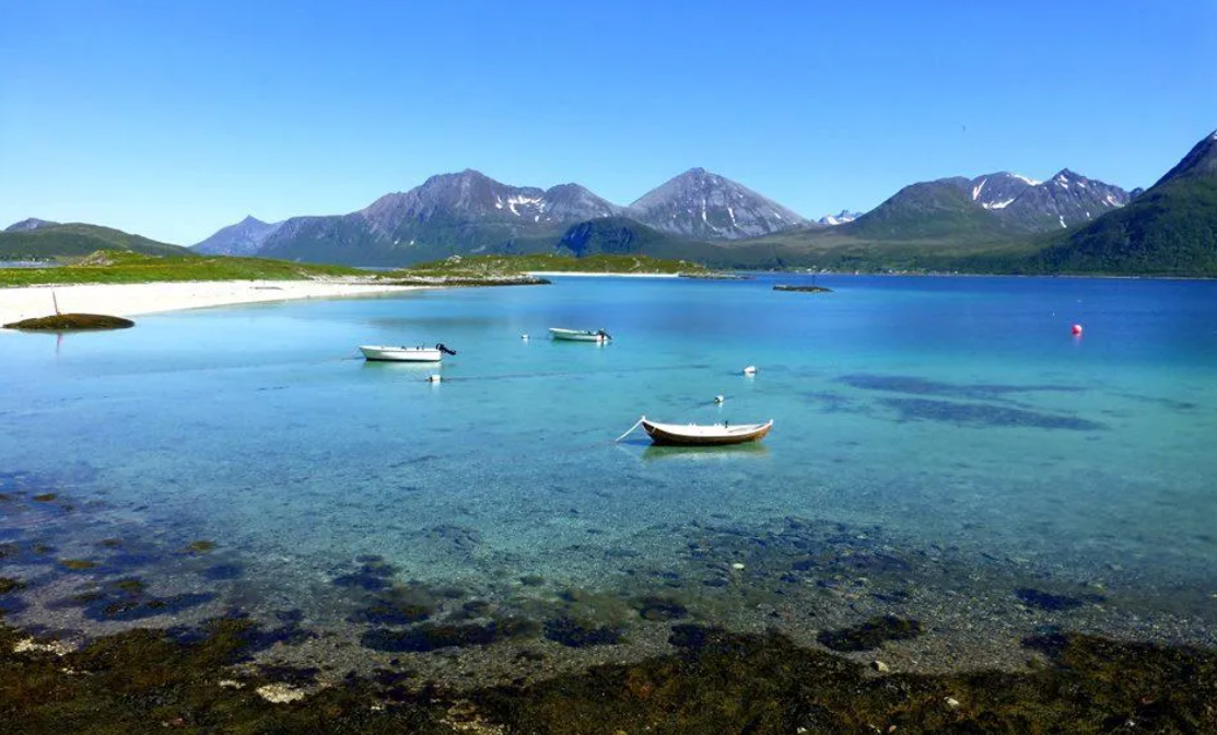 Norway Tromso fjord with turquoise water, white sandy beach, small boats, and rugged snow-capped mountains