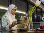 Novotel Makkah Thakher City guest in white hijab reading a newspaper while holding a green cup