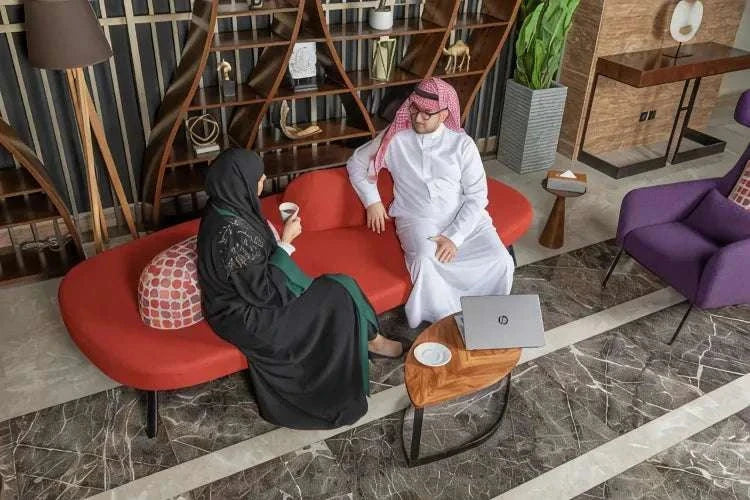 Novotel Makkah Thakher City lounge with guests in traditional attire seated on a red sofa beside a laptop