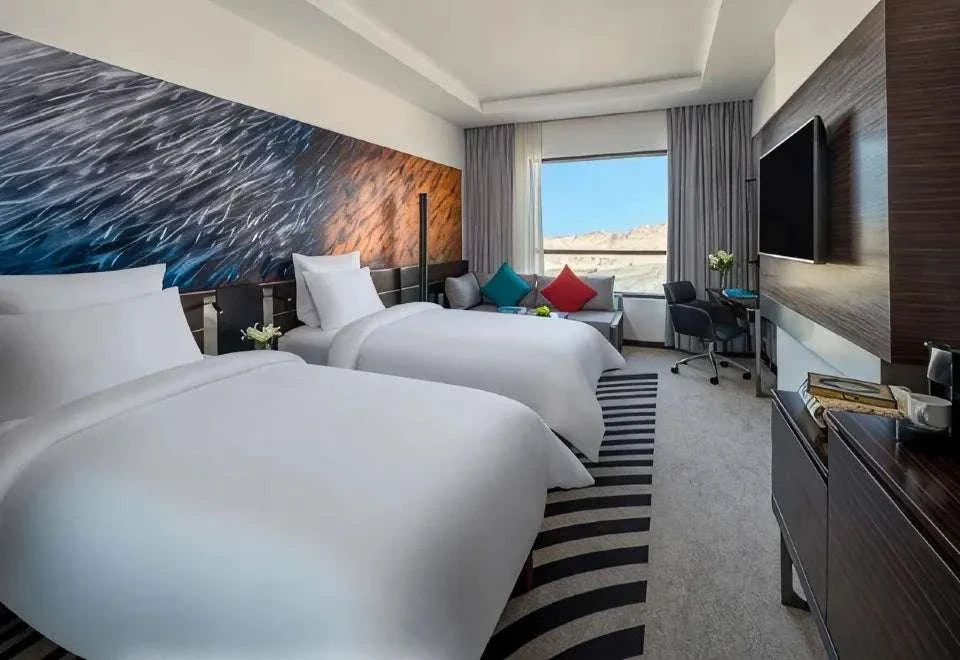 Novotel Makkah Thakher City hotel room with two white beds, colourful cushions, abstract wall art and television