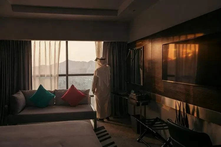 Novotel Makkah Thakher City hotel room with modern dark wood interior, sofa, colourful cushions, TV and window